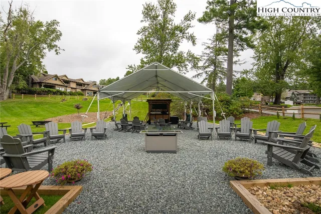 a view of a backyard with couches table and chairs under an umbrella with large trees