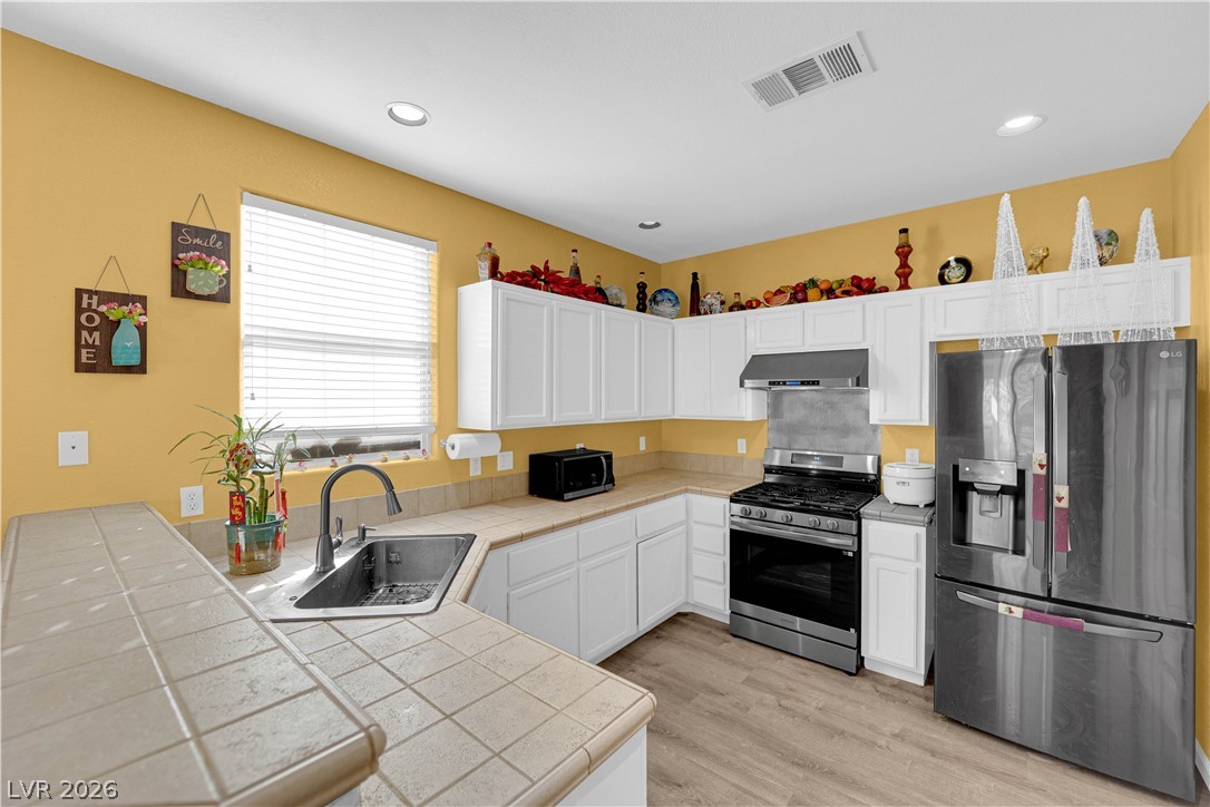 8170 West Festuca Way Las Vegas, NV 89113 - Photo 12 of 29 Kitchen with stainless steel appliances, a peninsula, white cabinets, light wood finished floors, and tile counters