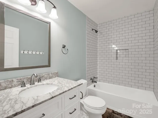 a bathroom with a granite countertop bathtub shower sink vanity mirror and toilet