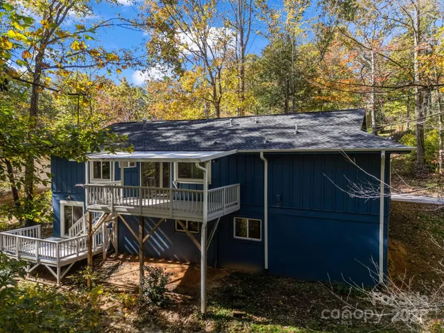 a view of a wooden house with a small yard and large trees