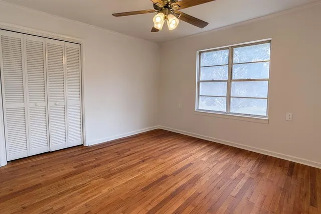 an empty room with wooden floor chandelier fan and windows