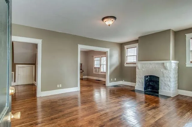 an empty room with wooden floor fireplace and windows