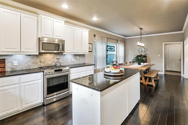 a kitchen with stainless steel appliances granite countertop a stove a sink dishwasher a microwave oven and a dining table with wooden floor