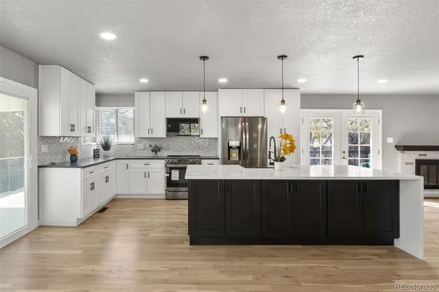 a kitchen with stainless steel appliances granite countertop a refrigerator a sink dishwasher a stove and white cabinets with wooden floor