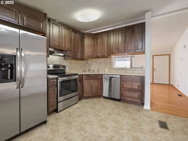 a kitchen with stainless steel appliances granite countertop a stove a refrigerator and a sink with wooden cabinets