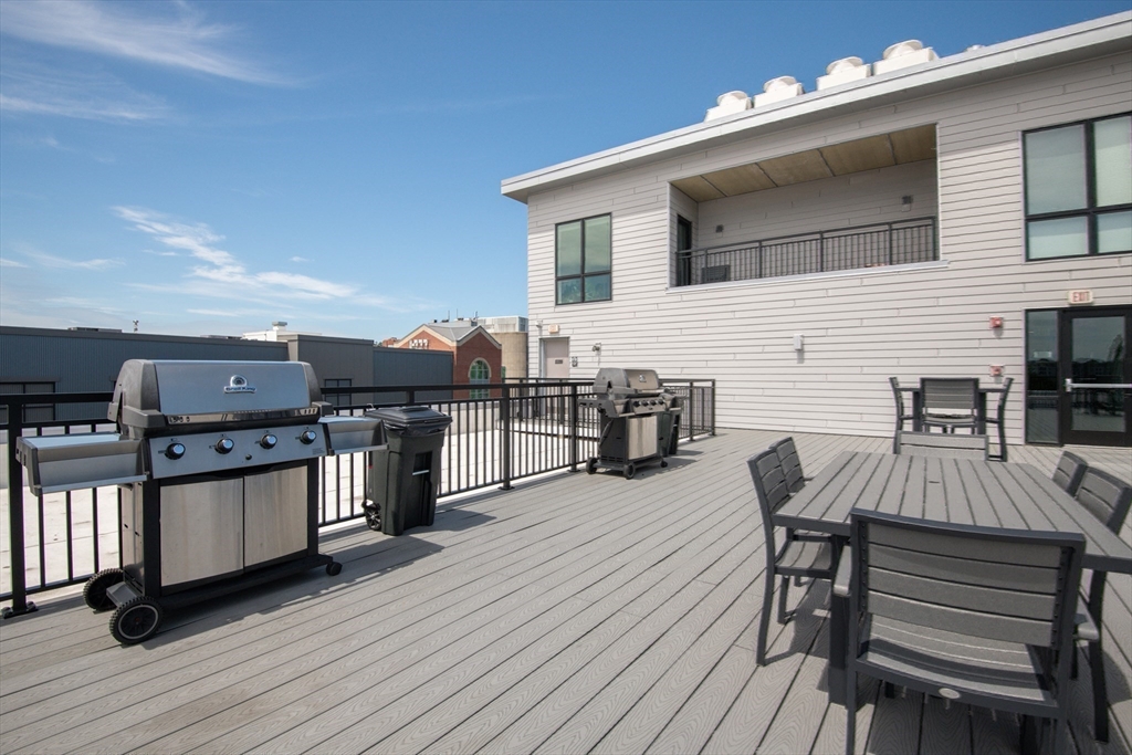 3531 Washington Street, Unit 316 Boston, MA 02130 - Photo 31 of 40 a view of a roof deck with table and chairs a barbeque with wooden floor and fence