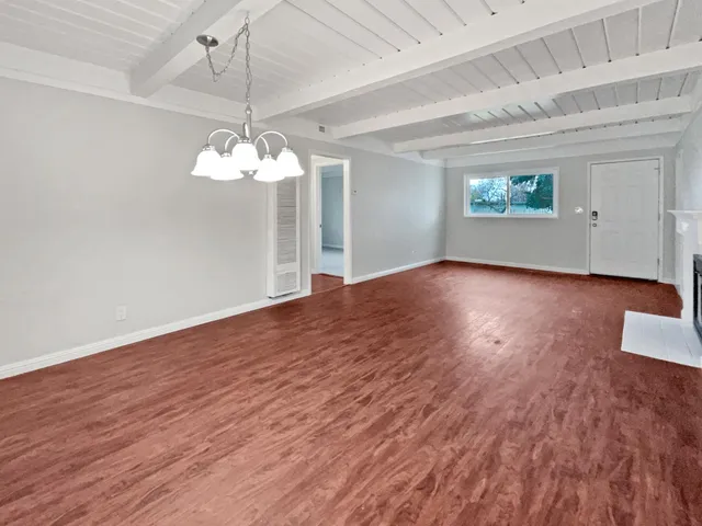 an empty room with wooden floor chandelier fan and windows