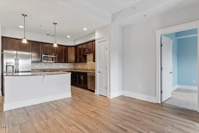 a kitchen with stainless steel appliances granite countertop a refrigerator a sink dishwasher a stove and white countertops with wooden floor