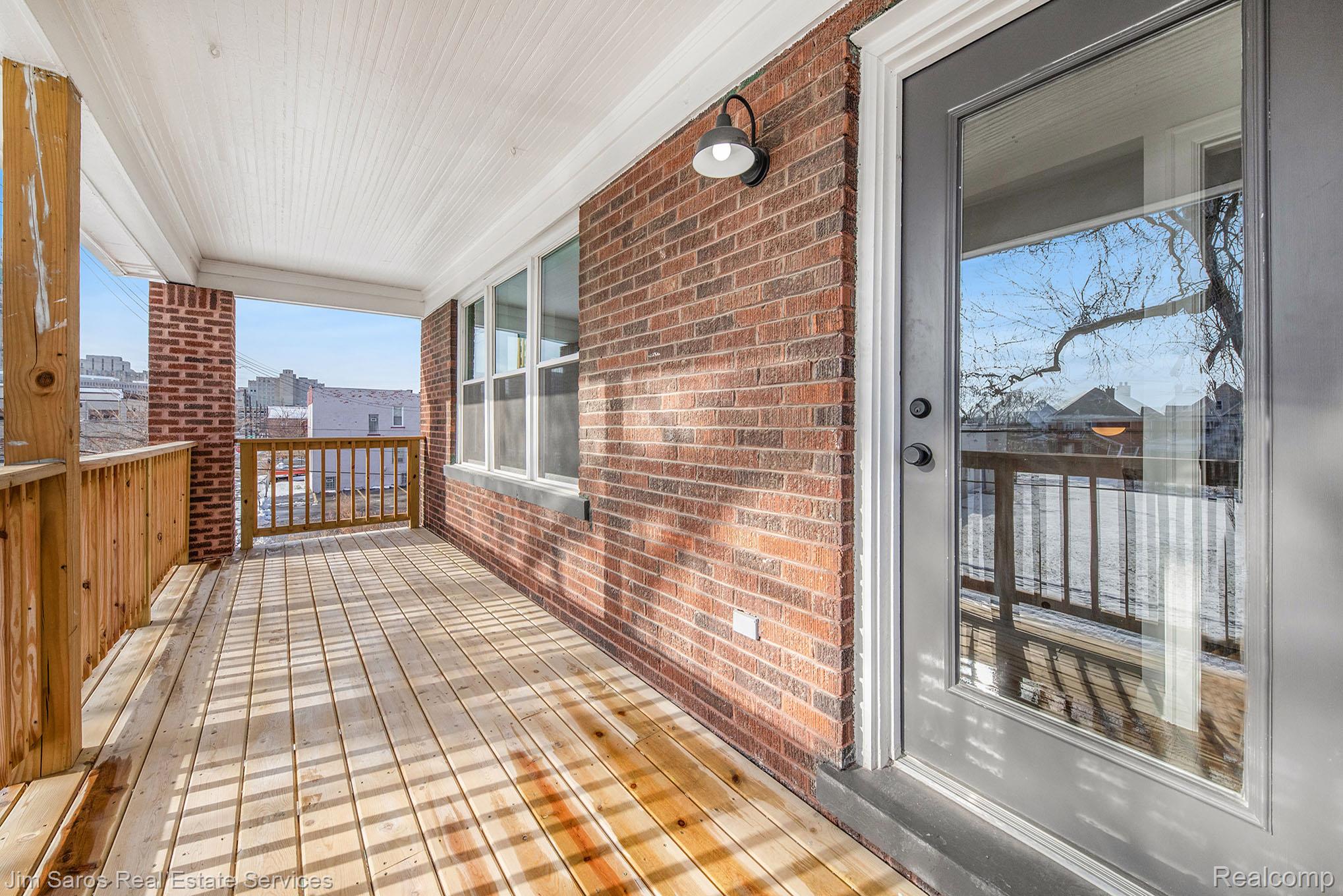 249 Custer Street Detroit, MI 48202 - Photo 20 of 22 Covered outdoor porch featuring wood-finish decking, brick facade, white beadboard ceiling, wood railings, and a full-light entry door