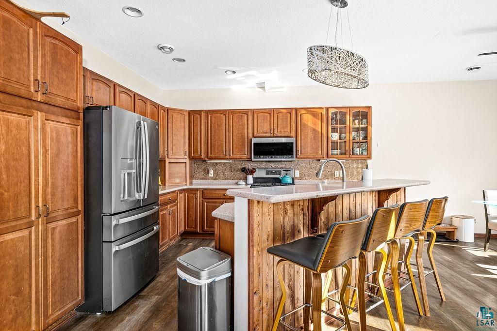 6048 Lakewood Road Duluth, MN 55804 - Photo 24 of 65 Kitchen with dark wood-style flooring, stainless steel appliances, brown cabinetry, backsplash, and glass insert cabinets