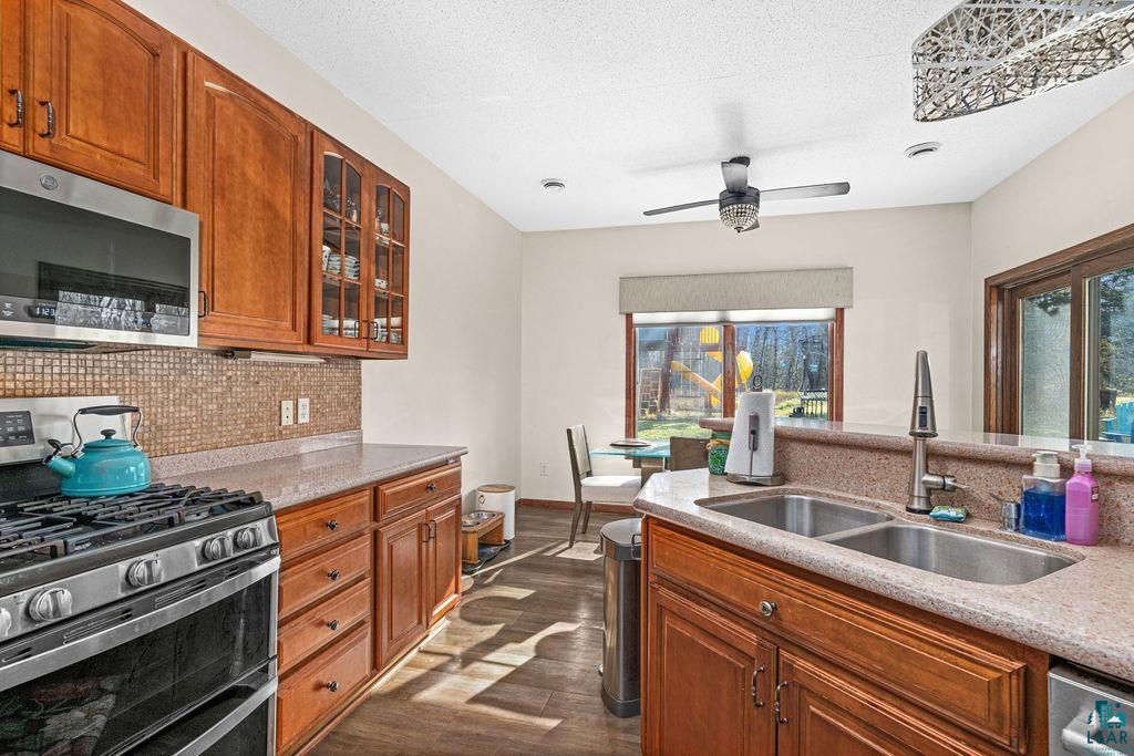 6048 Lakewood Road Duluth, MN 55804 - Photo 31 of 65 Kitchen featuring stainless steel appliances, brown cabinets, light stone counters, dark wood-type flooring, and decorative backsplash