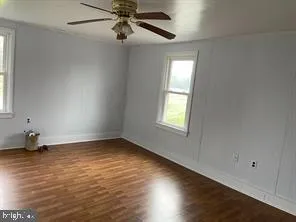 an empty room with wooden floor chandelier fan and windows