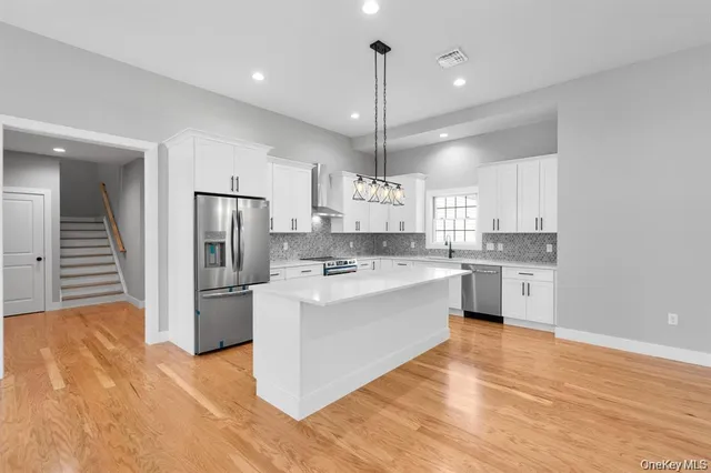 a large kitchen with kitchen island a stove a sink dishwasher a refrigerator and white cabinets with wooden floor