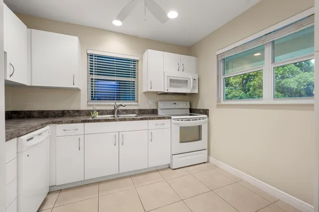 a kitchen with granite countertop white cabinets white appliances a sink and a window