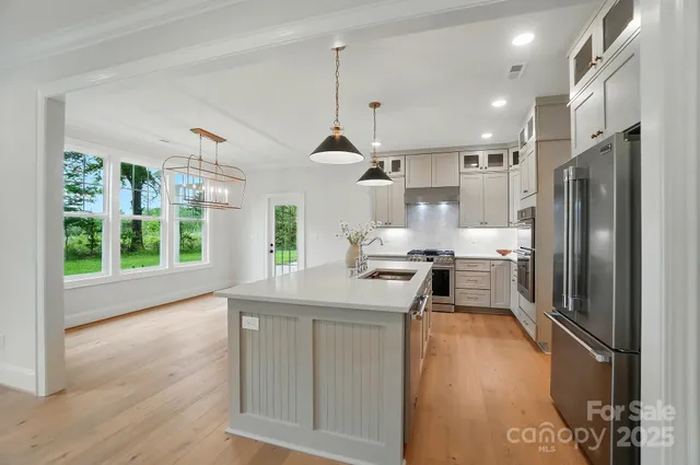 a kitchen with stainless steel appliances granite countertop a refrigerator a sink dishwasher a stove and a dining table with wooden floor