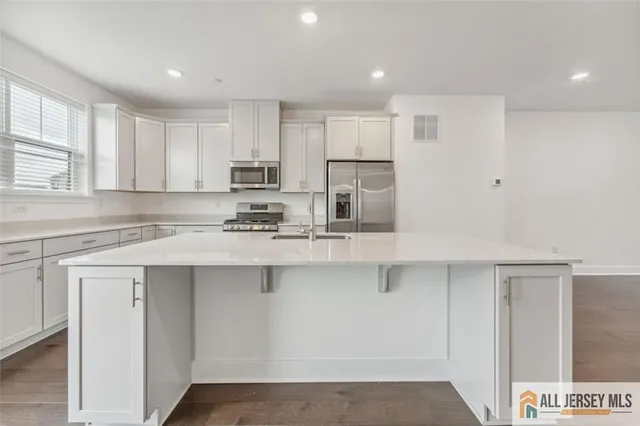 a kitchen with stainless steel appliances granite countertop a sink a stove a refrigerator and white cabinets