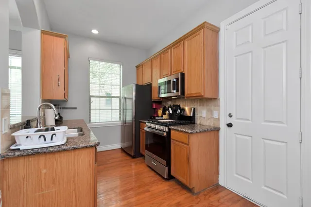 a kitchen with stainless steel appliances granite countertop a stove top oven a sink dishwasher and a refrigerator with wooden floor