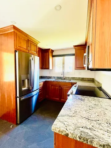a kitchen with stainless steel appliances granite countertop a refrigerator a stove and a sink with wooden cabinets