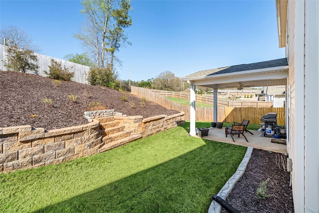 216 Carvel Trail Seneca, SC 29678 - Photo 42 of 46 This private outdoor living space features a covered patio and a tiered retaining wall leading to a fenced yard.