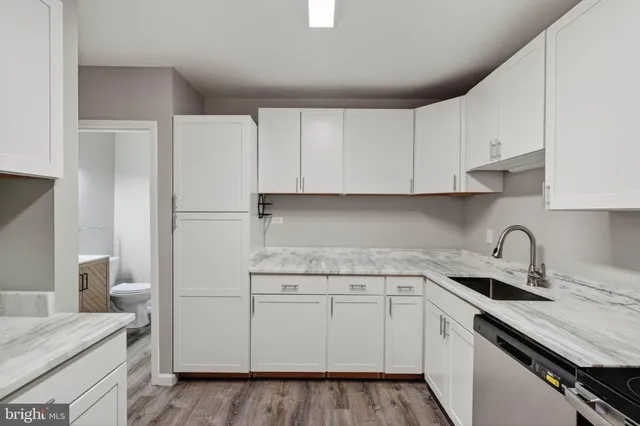 a kitchen with a sink dishwasher and white cabinets with wooden floor