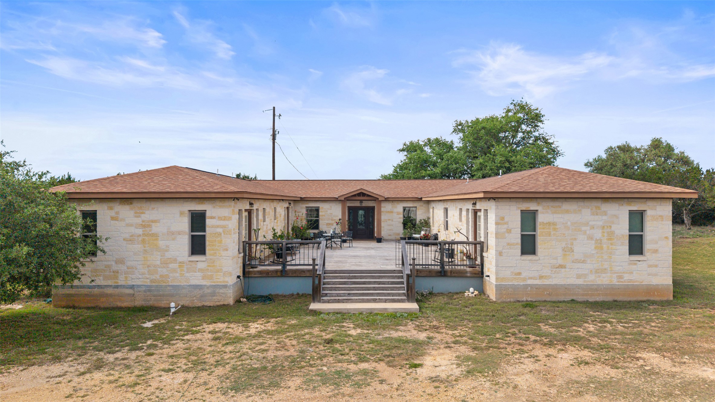 2966 Rm 165 Dripping Springs Dripping Springs, TX 78620 - Photo 12 of 23 Expansive single-story residence with a stone veneer exterior, a large elevated deck with wood railing, and a brown shingle roof