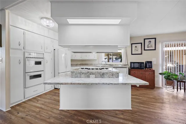 a large kitchen with stainless steel appliances granite countertop a stove a refrigerator a oven and white cabinets with wooden floor