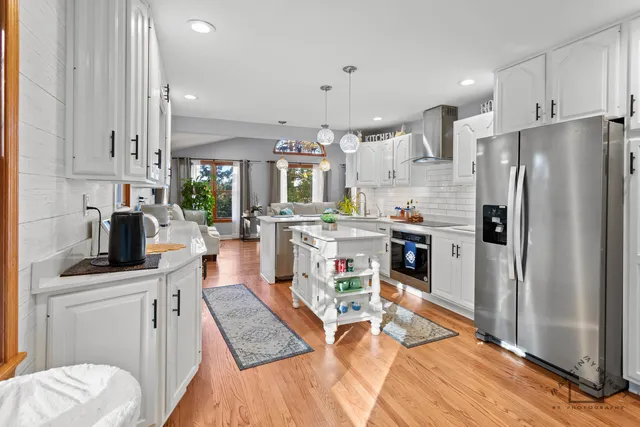 a kitchen with stainless steel appliances granite countertop a refrigerator a sink dishwasher a stove top oven a dining table and chairs with wooden floor