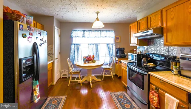 a kitchen with stainless steel appliances granite countertop a stove a refrigerator a sink dishwasher a dining table and chairs with wooden floor