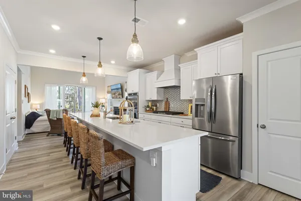 a kitchen with stainless steel appliances a refrigerator a stove a sink a dining table and chairs with wooden floor