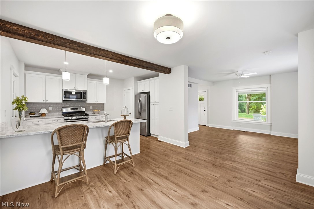 272 Miles Road Chagrin Falls, OH 44022 - Photo 10 of 36 Open-concept living area featuring wood style flooring, a kitchen island with granite countertop, stainless steel appliances, white cabinetry, and a wood beam accent