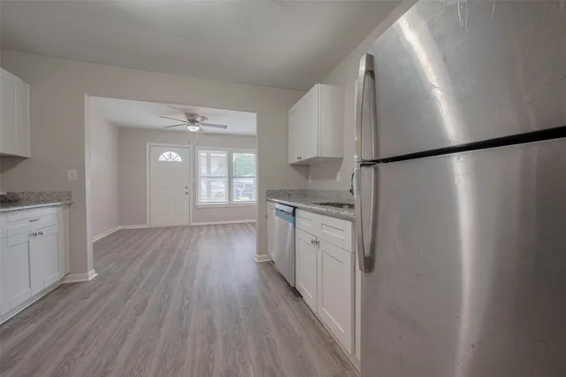 a kitchen with stainless steel appliances granite countertop a refrigerator a sink and white cabinets with wooden floor