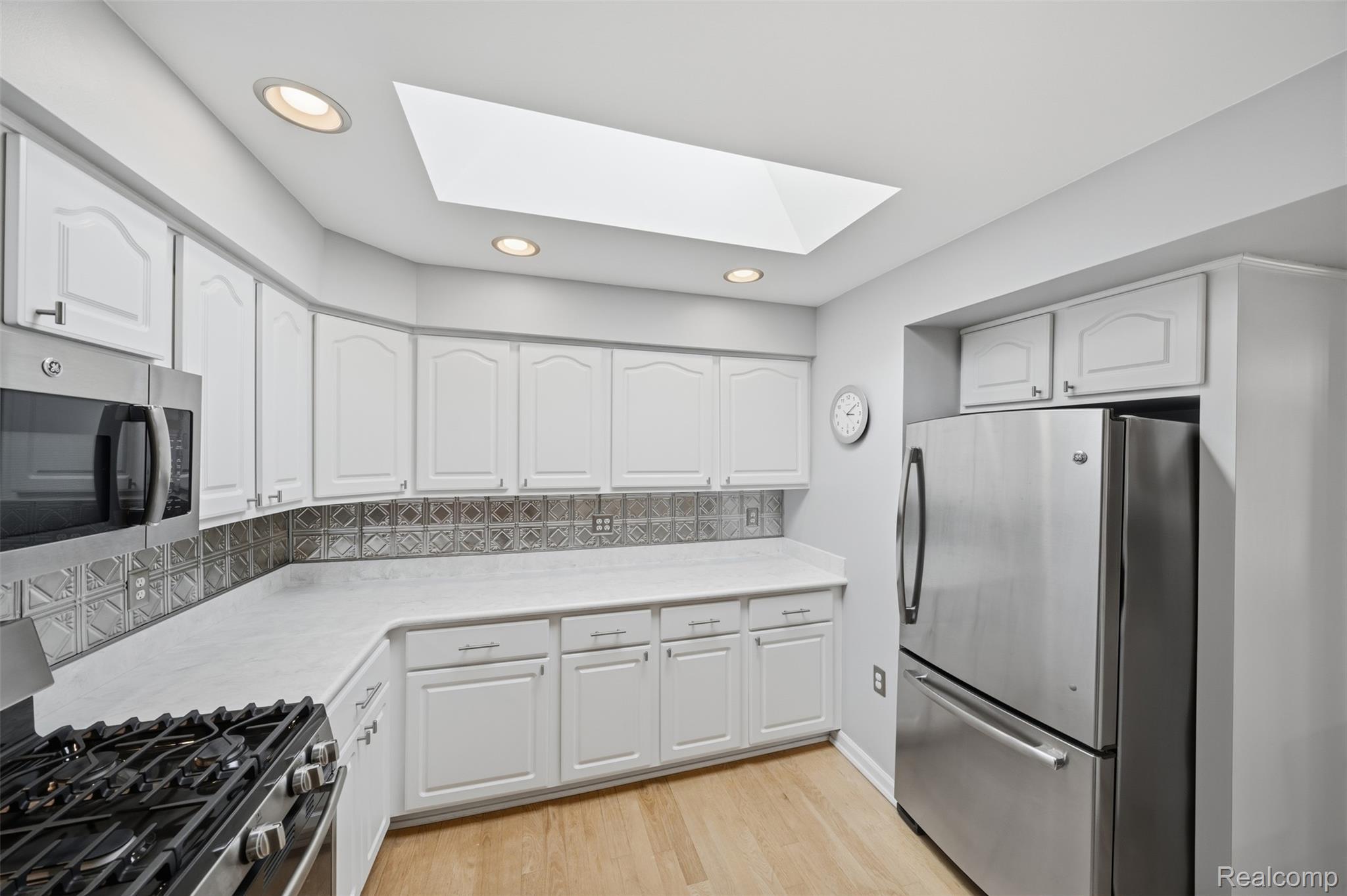 1087 Collingwood Drive Rochester, MI 48307 - Photo 11 of 56 White cabinetry with chrome hardware, an integrated skylight, recessed lighting, stainless steel appliances, and wood-finish flooring