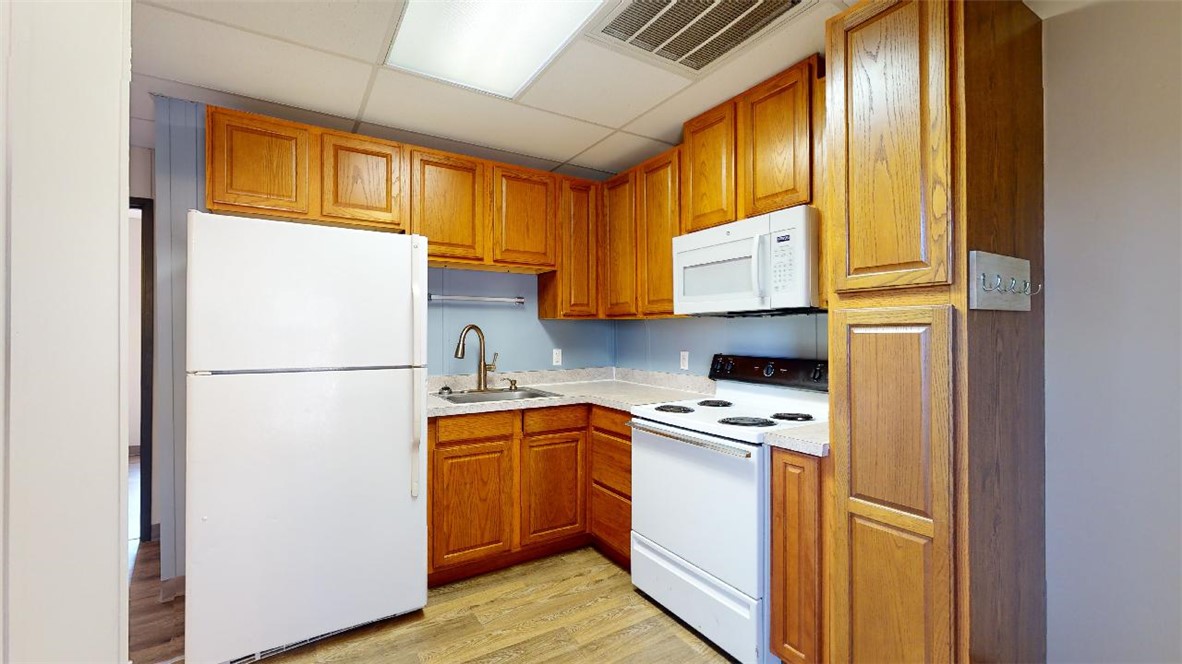 5585 Straub Road, Unit 110 College Station, TX 77845 - Photo 5 of 14 Kitchen with white appliances, a paneled ceiling, light countertops, brown cabinetry, and light wood-style floors