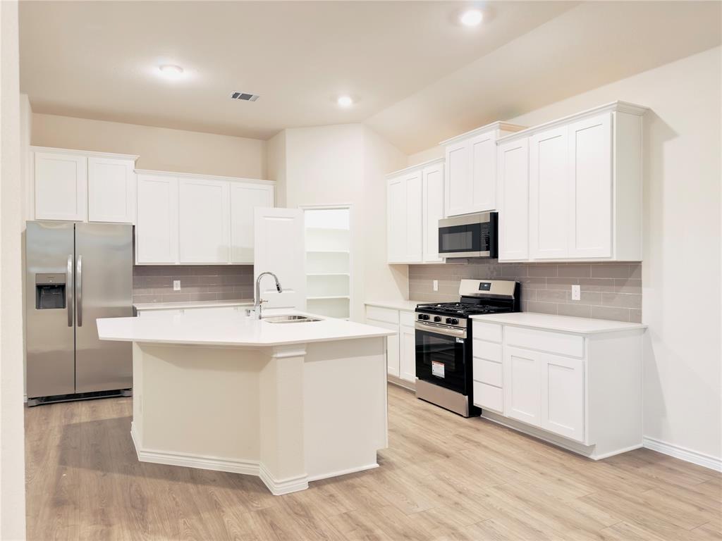 2117 Eugene Street Anna, TX 75409 - Photo 12 of 31 Kitchen with stainless steel appliances, white cabinetry, a kitchen island with sink, light wood finished floors, and decorative backsplash
