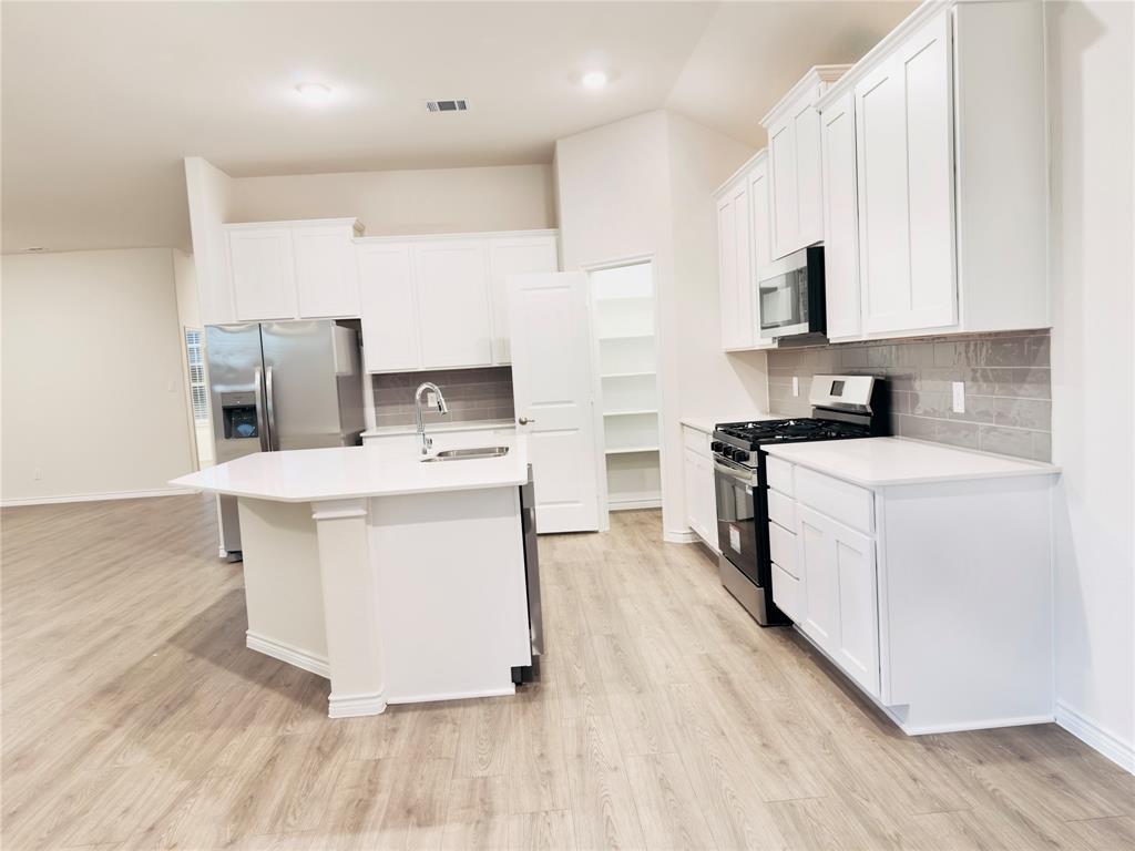 2117 Eugene Street Anna, TX 75409 - Photo 27 of 31 Kitchen featuring stainless steel appliances, white cabinetry, light wood-type flooring, and a center island with sink