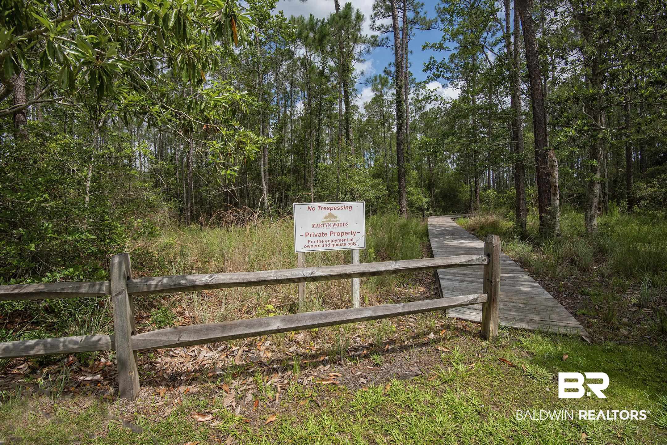 18754 Treasure Oaks Road Gulf Shores, AL 36542 - Photo 48 of 53 Wood fence entry featuring a natural wood boardwalk extending into a tree-lined landscape