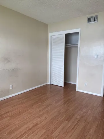 a view of an empty room with wooden floor and closet