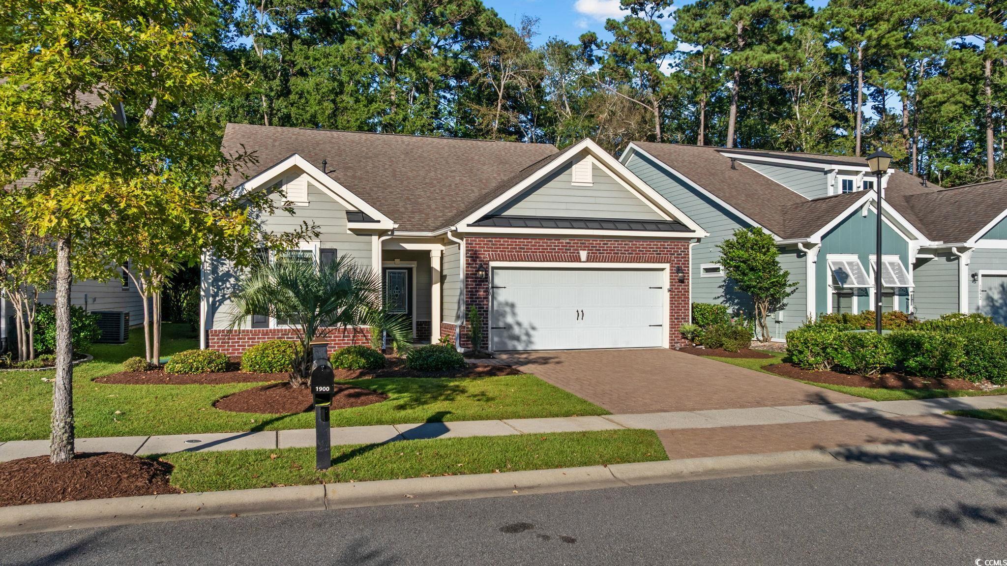 View of front of house featuring brick siding, decorative driveway, a standing seam roof, a shingled roof, and a front yard