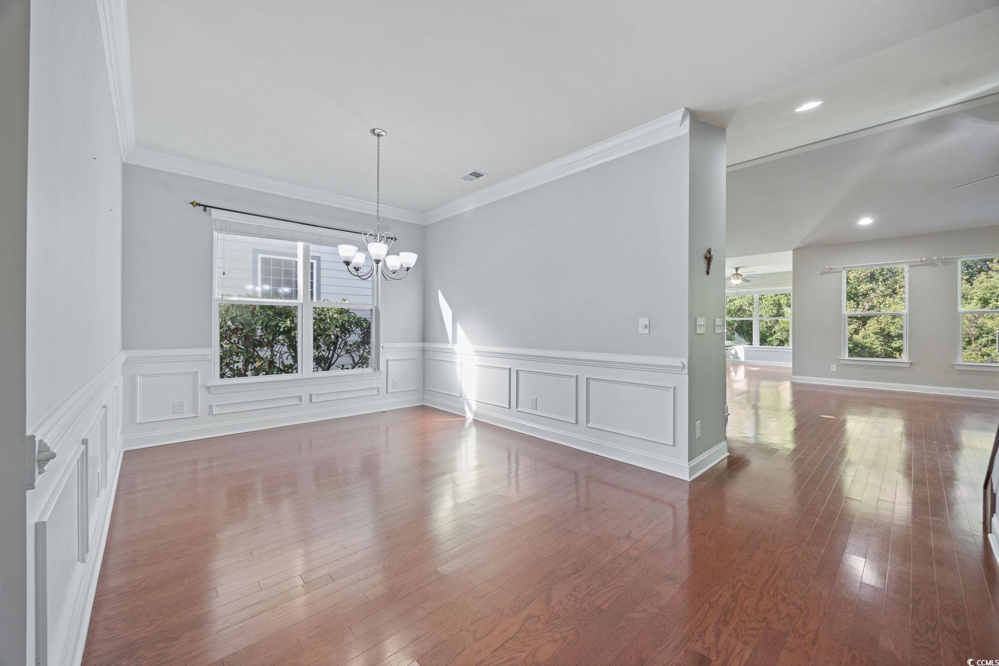 1900 Bluff Drive Myrtle Beach, SC 29577 - Photo 3 of 38 Unfurnished dining area with crown molding, dark wood-style flooring, a chandelier, ceiling fan, and a wainscoted wall