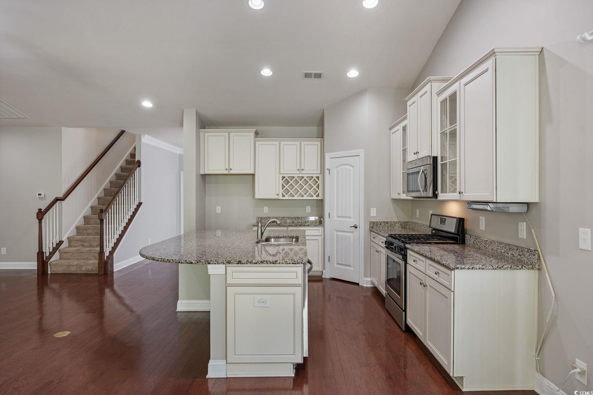 1900 Bluff Drive Myrtle Beach, SC 29577 - Photo 7 of 38 Kitchen with stainless steel appliances, glass insert cabinets, a center island with sink, light stone counters, and dark wood finished floors