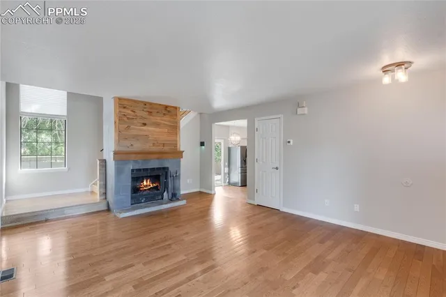 an empty room with wooden floor fireplace and windows