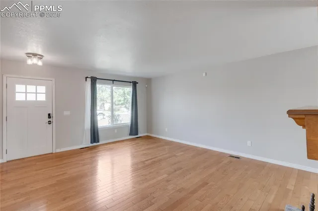 a view of an empty room with wooden floor and a window