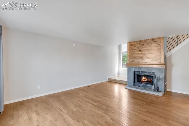 a view of an empty room with wooden floor fireplace and a window