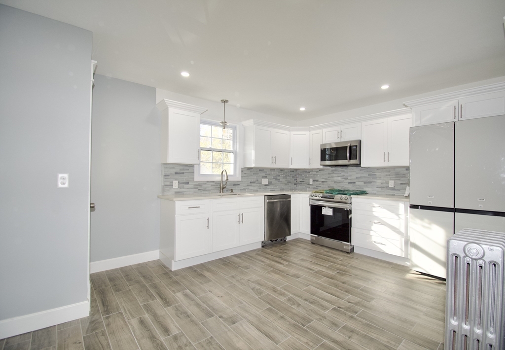 158 Gilbert Avenue Springfield, MA 01119 - Photo 9 of 30 a large kitchen with granite countertop a stove top oven a sink dishwasher a refrigerator and white cabinets with wooden floor