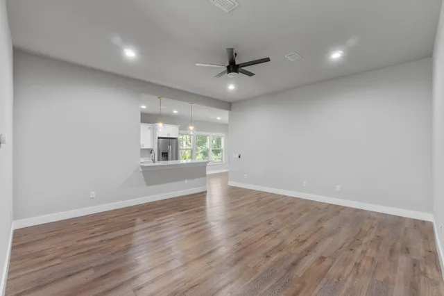 a view of an empty room and kitchen with wooden floor and a window