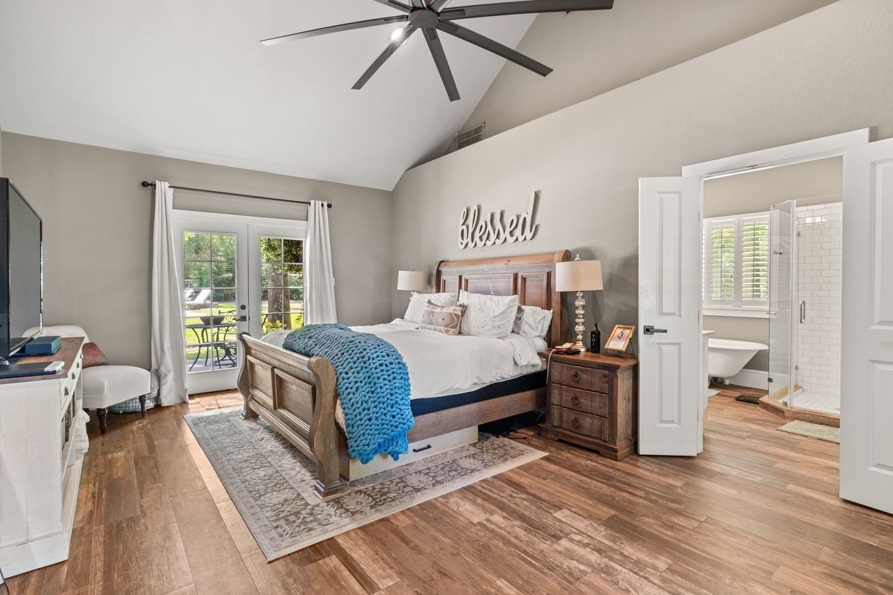 36 Wind River Drive Conroe, TX 77384 - Photo 27 of 45 This is the primary bedroom downstairs. This spacious bedroom features a vaulted ceiling, elegant wood flooring, and abundant natural light from large glass doors leading to an outdoor patio. The room includes a cozy seating area and an en-suite bathroom with modern fixtures.
