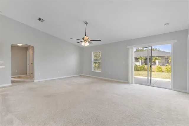 a view of an empty room with chandelier fan and windows