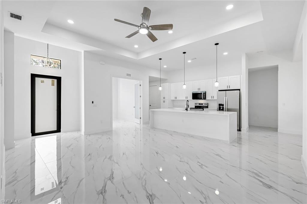 Unfurnished living room with a ceiling fan, recessed lighting, a high tray ceiling, and light marble finish floors