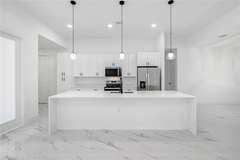 2113 Grayson Avenue Alva, FL 33920 - Photo 5 of 25 Kitchen featuring stainless steel appliances, light stone counters, decorative light fixtures, white cabinetry, and a spacious island