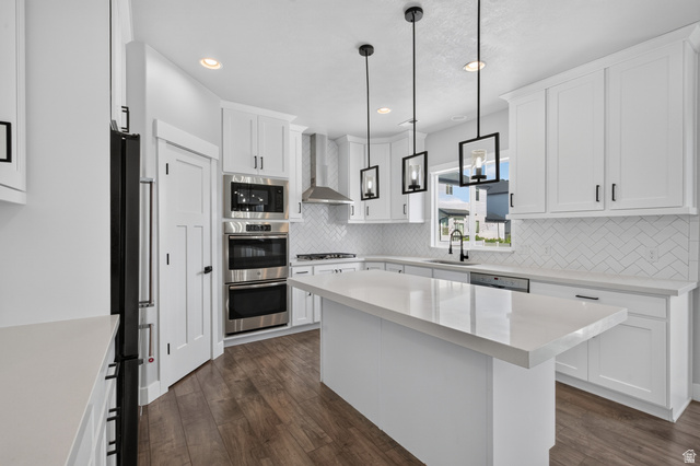 36 West Syracuse Road Vineyard, UT 84059 - Photo 16 of 56 Contemporary kitchen featuring an oversized island with a solid surface countertop, white shaker cabinetry, stainless steel appliances, herringbone tile backsplash, and wood-finish flooring